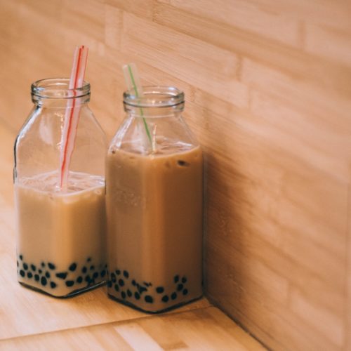 Two clear glass jars of coconut boba tea with straws