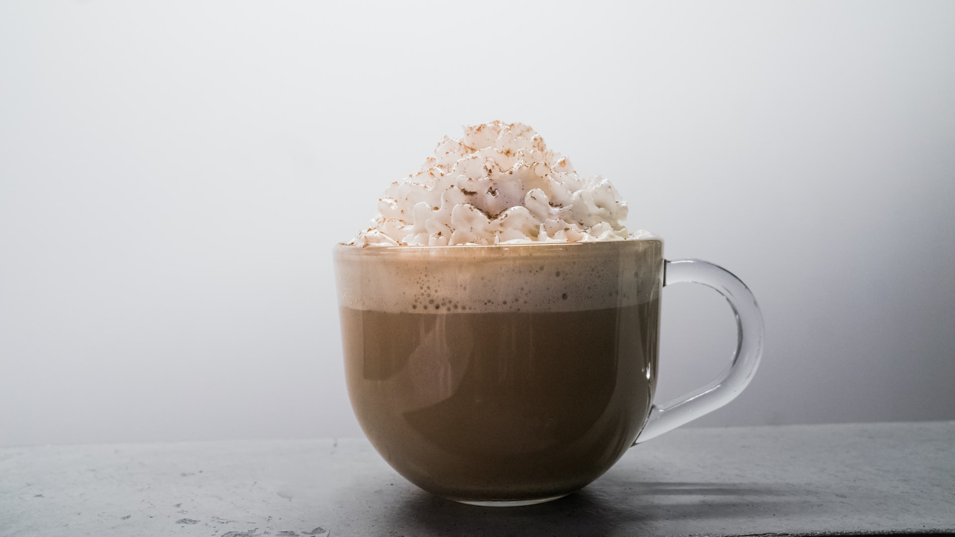 Transparent mug of coffee with whipped cream